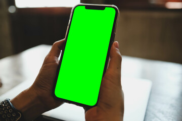 A person's hands holding a modern smartphone with a blank green screen. A perfect chroma key mockup for showcasing mobile apps or video content.