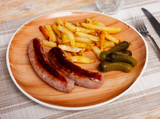 Fried sausages with served with french fries potatoes and marinated cucumbers