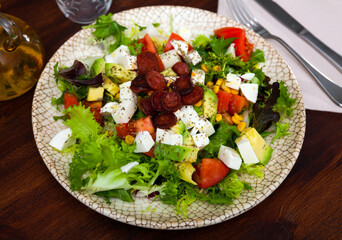 Refreshing salad with greens, tomatoes, avocado, corn, mozzarella and fried sausages