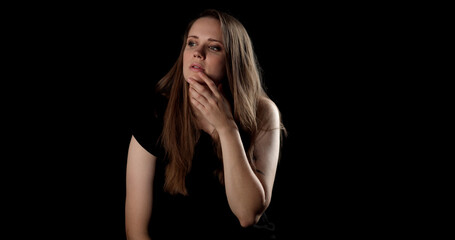 Studio portrait of a thoughtful young woman with hand on chin looking away on a dark background