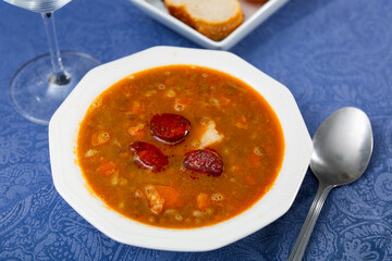 Spicy stewed lentils with suasage and vegetables with thick tomato sauce served in white plate. Typical Spanish cuisine