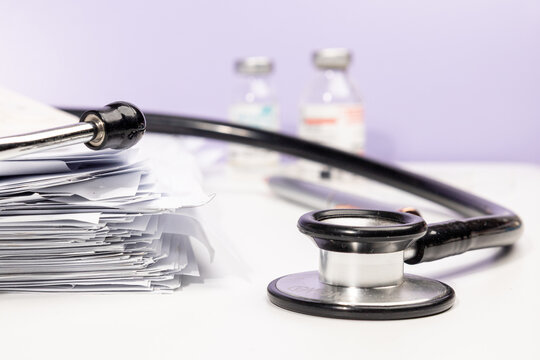 A neat stack of medical papers rests on a doctor’s desk, surrounded by essential medical tools such as a stethoscope and thermometer. This setup reflects a clinical documentation process in a hospital