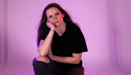Studio shot of a young woman crouching with a bored expression, resting her face on her hand
