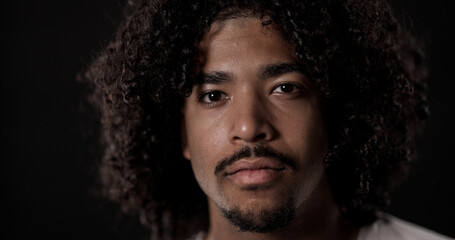 Close up portrait of a serious young African American man with curly hair and goatee posing on a...