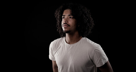 Portrait of a young african american man with curly hair and goatee looking up on a black background
