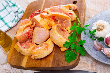 Fresh raw chopped chicken pieces on a wooden cutting board with a sprig of fresh parsley, garlic...
