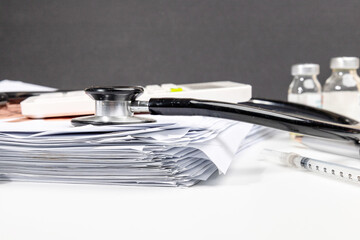 An organized pile of medical documents placed on a clinical workspace with medical instruments...