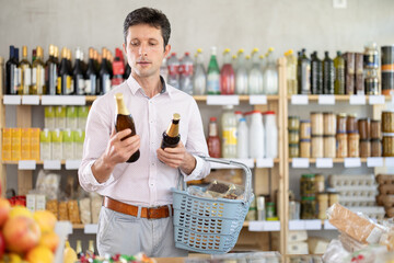 Man in a European supermarket chooses craft beer in dark glass bottles against the background of...
