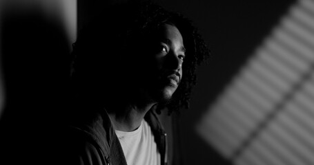 Dramatic black and white portrait of a thoughtful young African American man illuminated by window...