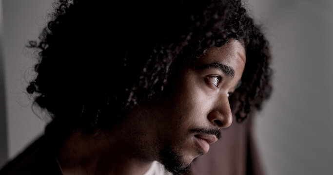Close up portrait of a thoughtful young african american man with curly hair looking away with hope