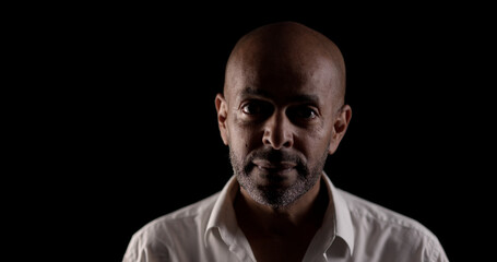 Studio portrait of a serious african american mid adult man wearing a white shirt on a black...