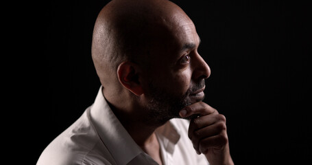 Profile of thoughtful businessman holding his chin, illuminated by dramatic lighting on a dark...