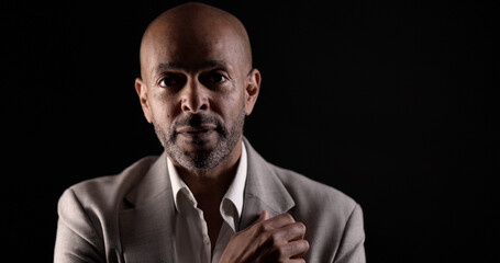 Portrait of a serious African American businessman adjusting his suit while posing on black...