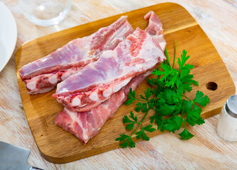 Fresh meaty pork ribs with condiments ready for cooking on wooden cutting board on table