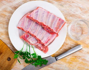 Raw meaty pork ribs slabs on plate with fresh greens ready for cooking ..