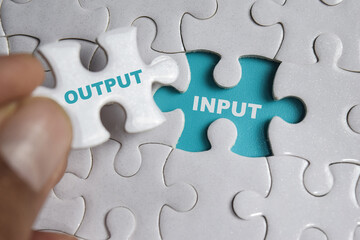 Hand holding piece of jigsaw puzzle with word Output or input. Business and finance concept