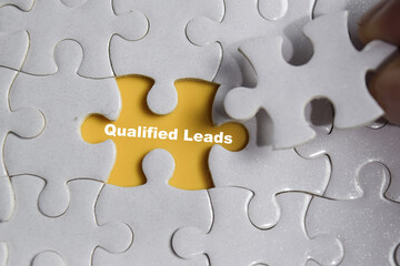 Hand holding piece of jigsaw puzzle with word Qualified leads. Business and finance concept