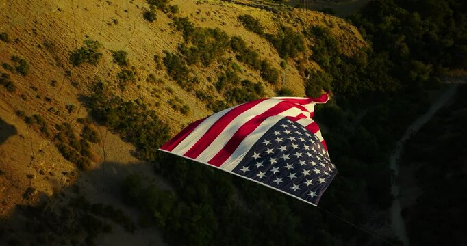 Epic, super slow motion drone shot over large rippling American flag at sunset