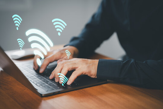 Businessman using laptop with floating Wi-Fi icons, symbolizing wireless internet connection, online communication, remote access, remote work, and network connectivity in a digital workspace.