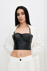 Young woman wearing a black leather corset top and white blazer, posing confidently with straight...