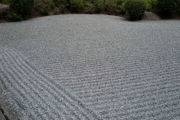 Close-up of a meticulously raked gravel surface in a Zen garden, showing textured parallel lines...