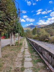 Stone pathway along a riverbank in a rural mountain landscape. Scenic walking trail next to a...
