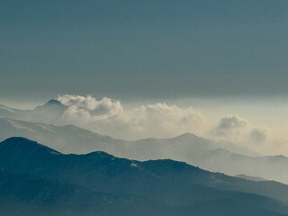 Misty mountain range landscape with layers of peaks and clouds. Serene blue haze creating...