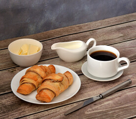 French breakfast, fresh croissants, black coffee, cream and butter on wooden table.
