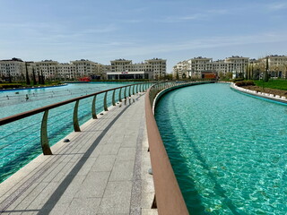 Curved walkway along a turquoise water canal in a modern city. Contemporary residential buildings...