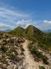 A narrow hiking trail winds along a scenic mountain ridge. Beautiful view of green hills and a blue sky on a sunny day. Outdoor adventure and travel concept.