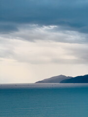 Calm turquoise sea with distant mountains under a dramatic cloudy sky. Scenic coastal landscape...