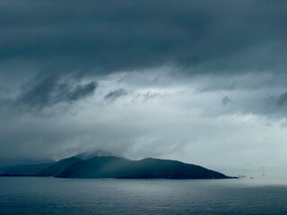 Moody seascape with a silhouetted island under a dark, stormy sky. Dramatic coastal landscape with...