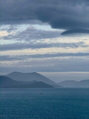 Moody seascape with layered mountains fading into the distance. Dramatic overcast sky over a vast...