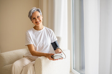 A mature elderly, well-groomed, beautiful woman pensioner with gray hair measures blood pressure