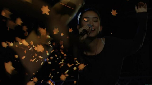 Singer stepping into concert spotlight and singing, activating amber confetti rain to audience
