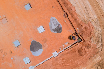 Heavy machinery works on foundation of new building at construction site with dirt gravel scattered...