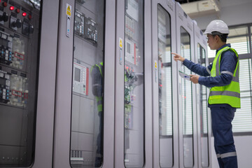 Engineer wearing safety helmet and reflective vest performs inspection on electrical relay panels...