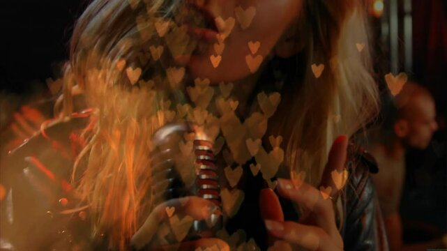 Camera pulling back showing singer at mic singing with strumming guitarist for music amid hearts
