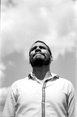 Bearded man looking up at cloudy sky in monochrome analog photo