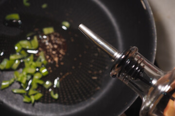 Cooking oil being drizzled over chopped herbs in skillet