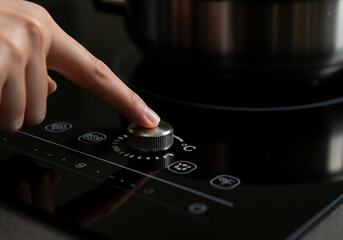Womans hand adjusting temperature on modern induction cooktop
