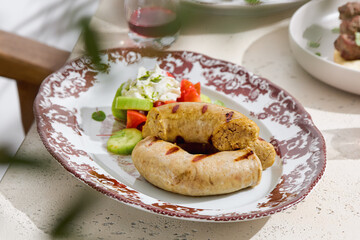 Grilled sausages with vegetable salad, bright natural light, closeup composition on vintage patterned plate