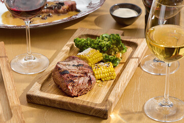 Filet mignon steak with grilled corn and broccoli, bright daylight, overhead wood tray composition