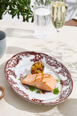 Grilled salmon steak with charred lemon, bright daylight, overhead composition on vintage-patterned plate