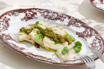 Grilled squid with chimichurri sauce on vintage plate, bright natural lighting, angled composition