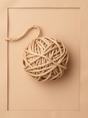A minimalist composition featuring a ball of natural twine on a beige background.