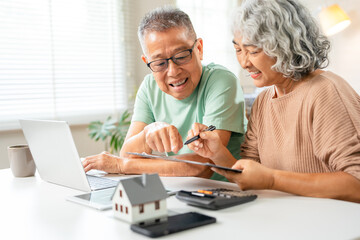 Happy senior couple reading important documents while sitting together at the table at home. Smiling mature spouses checking domestic bills before paying them online, discussing budget planning.