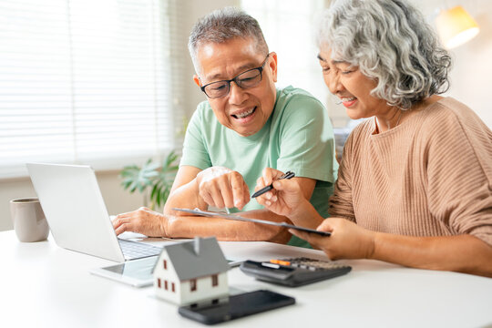 Happy senior couple reading important documents while sitting together at the table at home. Smiling mature spouses checking domestic bills before paying them online, discussing budget planning. - Powered by Adobe