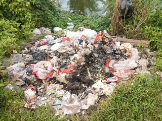 Burned Pile of Mixed Waste and Plastic Trash in Open Area Near River