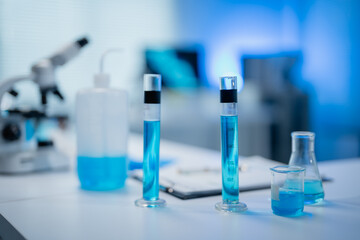 Laboratory setting featuring blue chemical solutions in glassware, including test tubes and beakers, with a microscope in the background, evoking a sense of scientific research and exploration